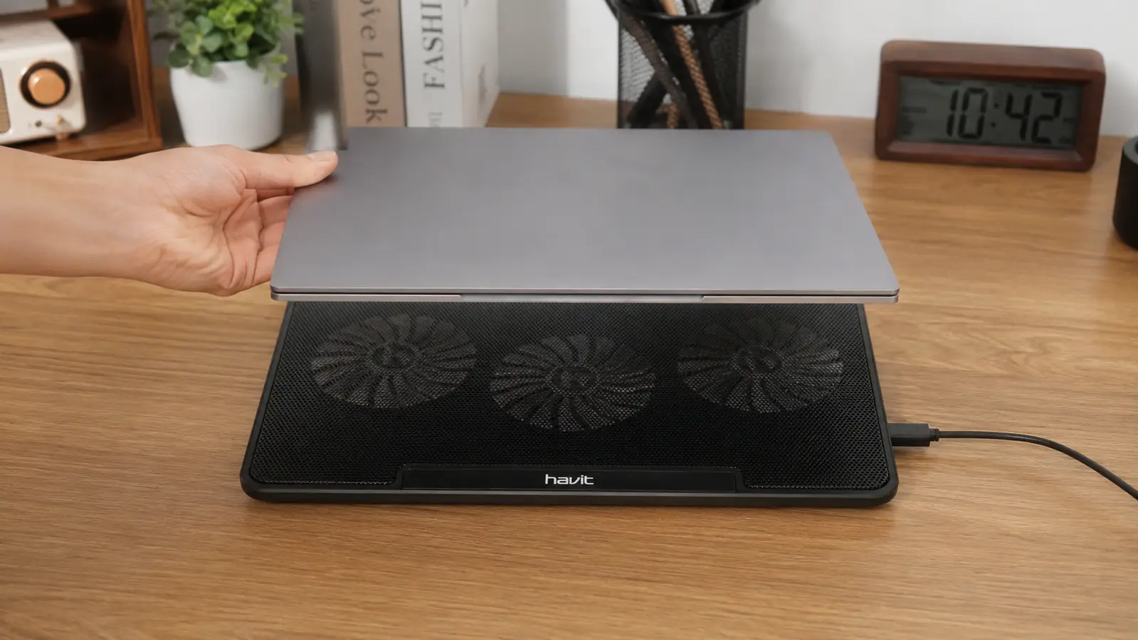 Hand setting a laptop down onto a cooling pad with the USB power cable already connected