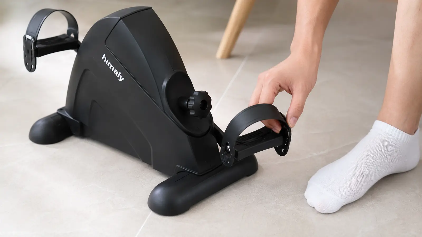 A close-up of a foot in an ankle sock buckling the strap on the himaly pedal exerciser pedal