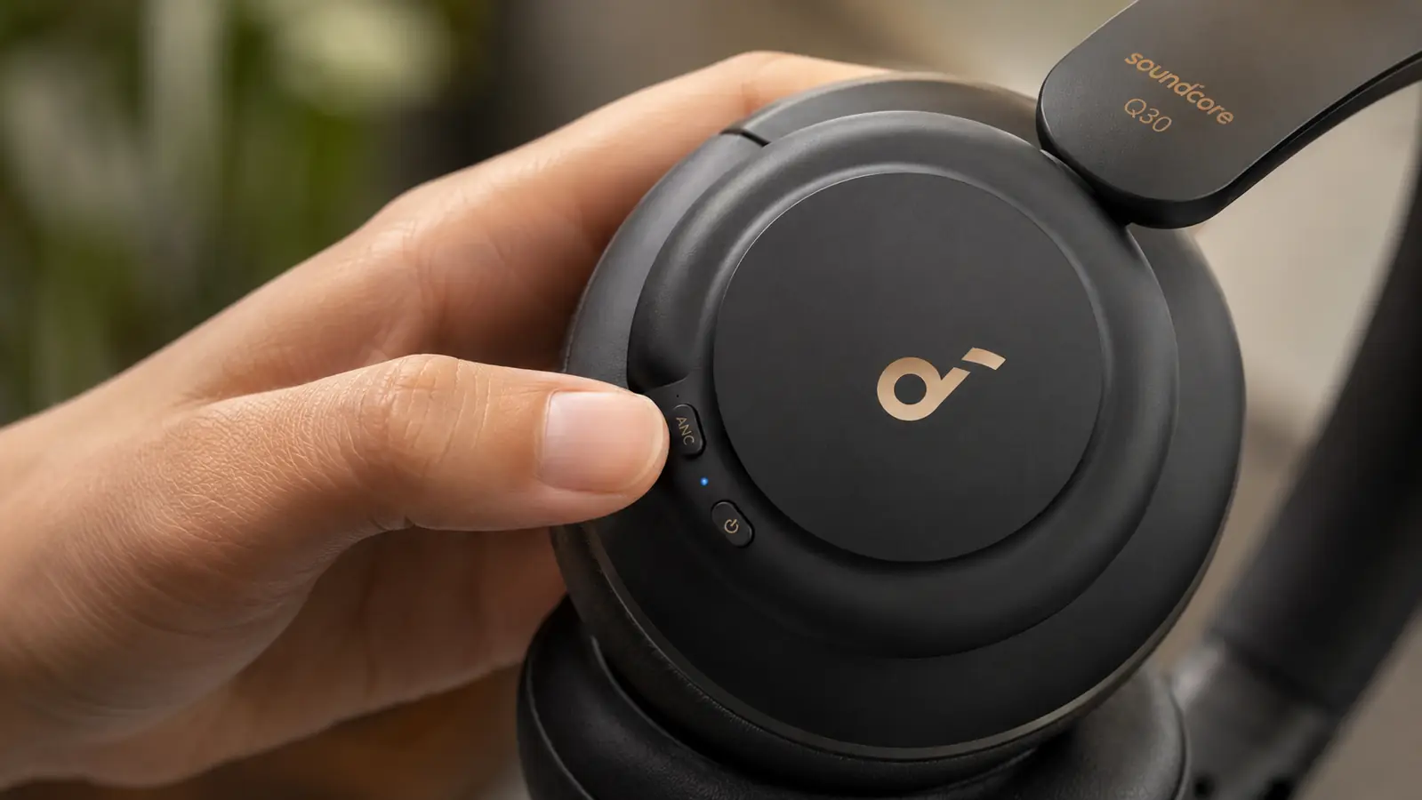 Close-up of hand adjusting the noise cancelling mode button on the ear cup of over-ear headphones