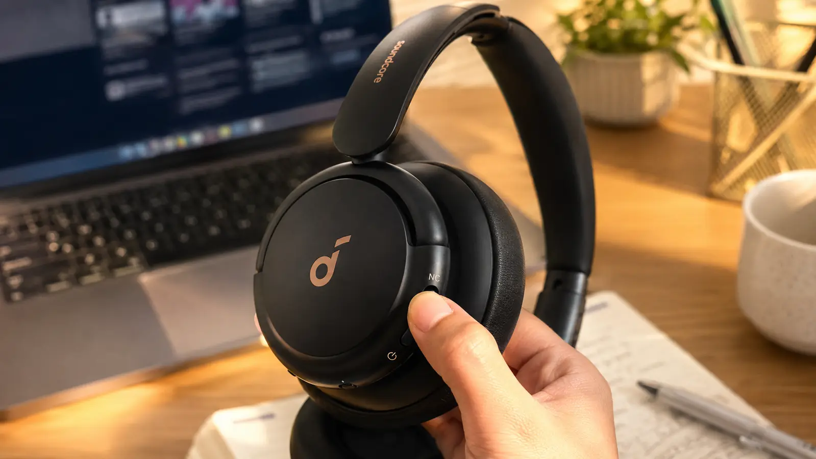 Hand adjusting the ANC mode button on the Soundcore Q30 headphones while sitting at a desk